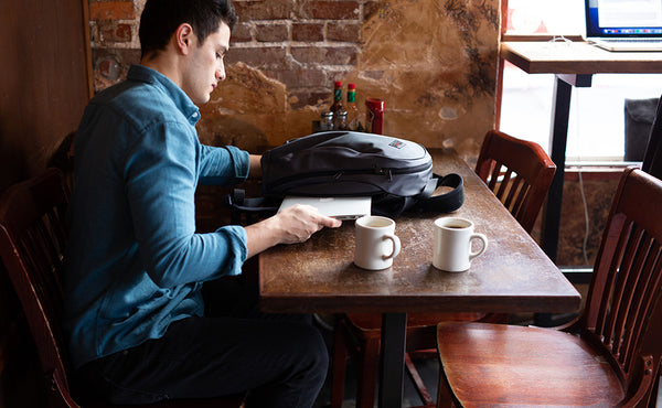 A person pulling their laptop out of the Luminary at a cafe.